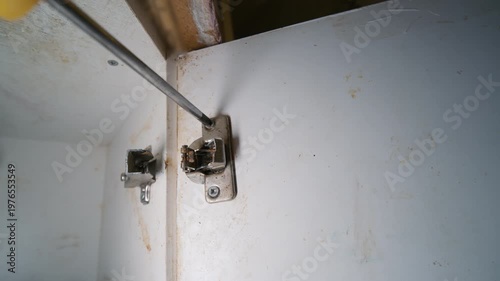 Screwdriver Removing Screw from Broken Cabinet Door Hinge | Damaged Silumin Kitchen Furniture Hardware Disassembly Close-Up | Home Repair and Renovation