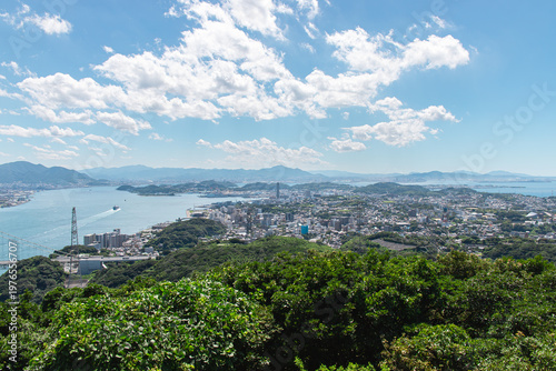 Elevated panoramic view of Shimonoseki, Yamaguchi Prefecture, showing the city's waterfront under a partly cloudy summer sky.