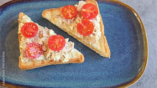 Tuna sandwich, tuna eggs salad sandwich with tomatoes on blue plate on grey table in cafe or restaurant, top view