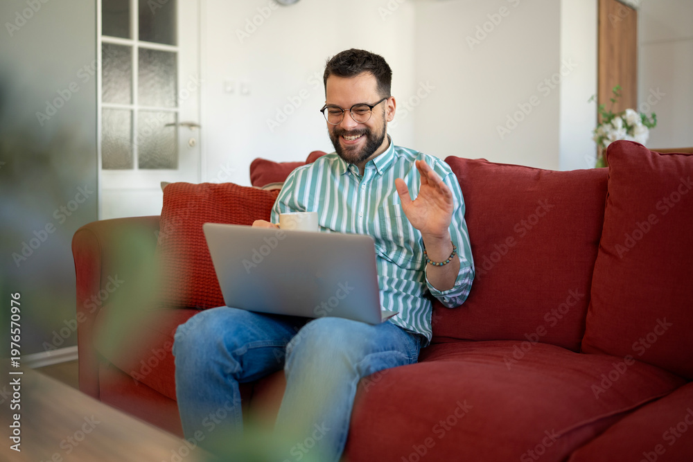 Obraz premium Smiling man waving during remote video conference at home