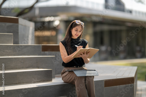 Woman writing notes in notebook sitting outdoors on stairs