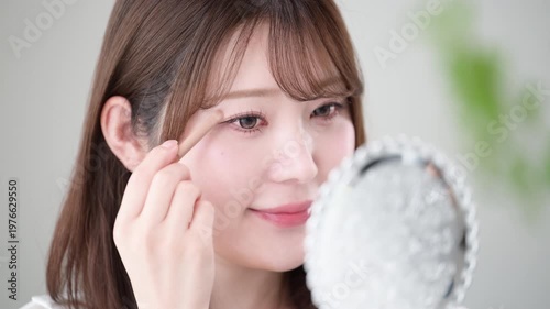 手鏡を見ながらアイシャドウを塗る女性のナチュラルメイクと美容ケアイメージクローズアップの動画　スローモーション