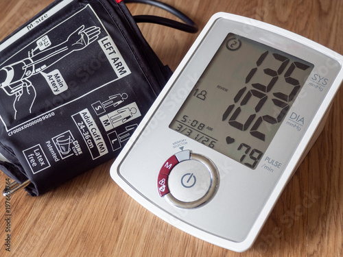 Digital blood pressure monitor with cuff on a wooden table showing high blood pressure reading