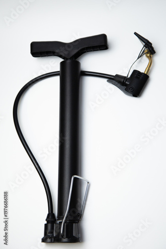 Vertical close-up photo of black pump hand pump with multiple attachments and leg handle lying on white background. High quality photo