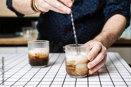 Canvas-taulu Person stirs coffee cocktail with metal bar spoon in ribbed glass on grid table