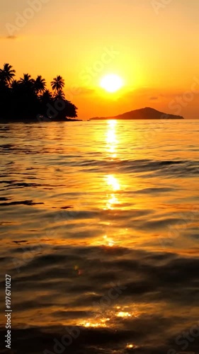 A beautiful golden sunset illuminates the calm ocean waves near a tropical island shore