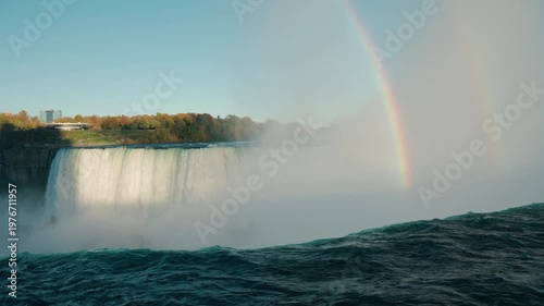 Niagara Falls with colorful rainbow forming in mist above powerful waterfall and flowing river water in scenic natural landscape