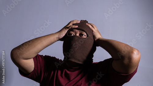 Bilde på lerret An adult male wearing a brown knit balaclava grabs his head with both hands in a dramatic pose of extreme frustration and stress
