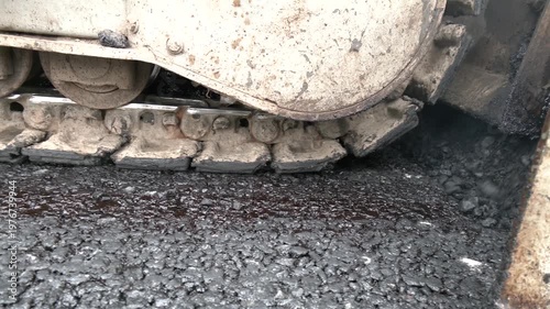 The equipment is spreading materials on the road to prepare for laying new asphalt. Worker operates an asphalt paving machine as it lays down fresh asphalt on roadway works