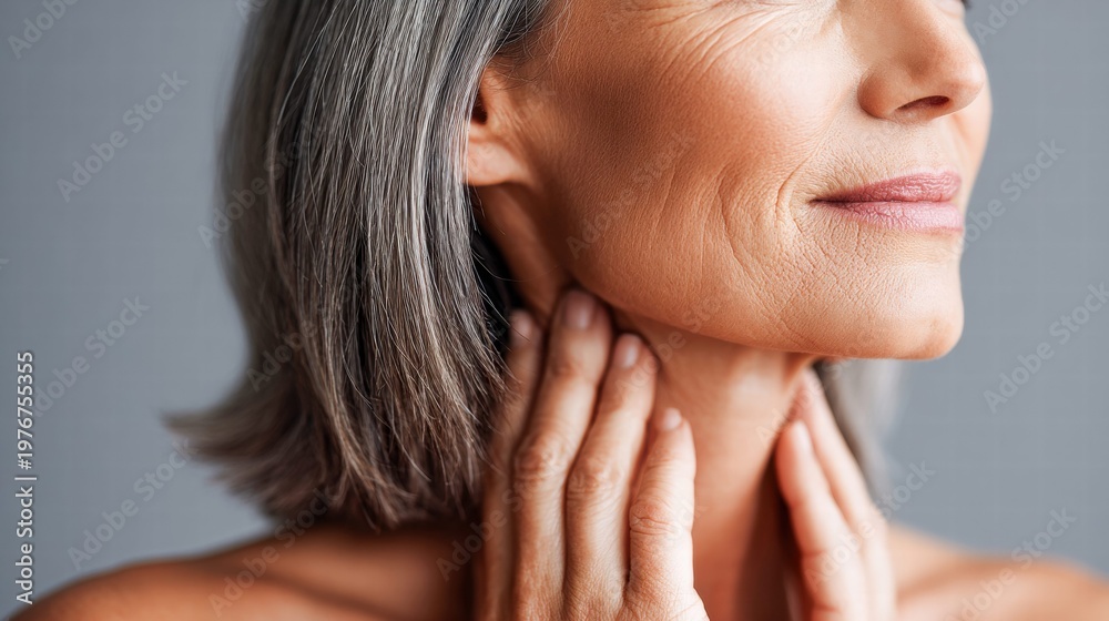 Fototapeta premium Mature woman gently touching her neck, showcasing aging gracefully.