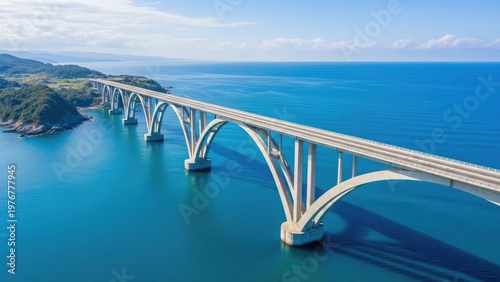 A long white bridge spans across a vast blue ocean under a clear sky
