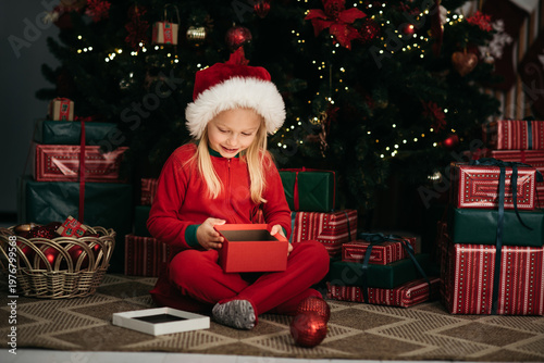 Merry Christmas and Happy Holidays. Little child under Christmas tree. baby girl in Santa Claus hat with gifts under Christmas tree with many gift boxes presents. Happy Holidays, New year.