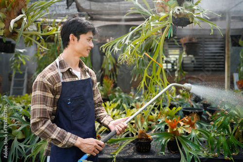 Konstfotografi A gardener with a watering hose and a sprayer water working in greenhouse and watering fern