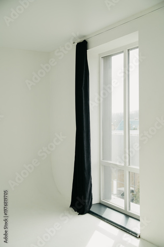Wide and large window with a black curtain in one of its parts on the wall in a white photo studio