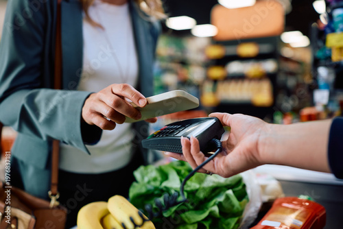 Foto Close up of woman paying with smart phone in supermarket.