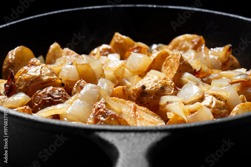Fried crispy chopped potato and onion cooked in a cast iron frying pan. On a black background backdrop