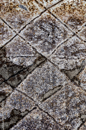 Close-up of a heavily weathered and rusted industrial metal surface. The image features a distinct square grid pattern with deep grooves, cracks, and a gritty metallic texture.  
