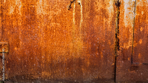 weathered metal garage doors with heavy orange corrosion and rust. The industrial iron gates meet a rough ground surface composed of aged concrete, grey gravel, and mineral debris 