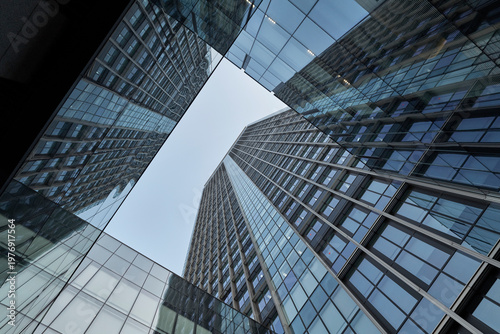 Looking up through reflective glass office towers to bright sky