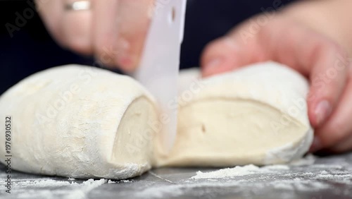 Hands of a person cutting and shaping dough on a floured surface, demonstrating the process of preparing bread in a cozy kitchen environment