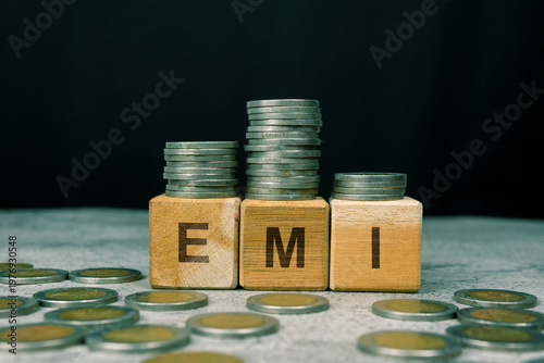 EMI word on a wooden cube with a stack of coins. Financial Investment Concept.