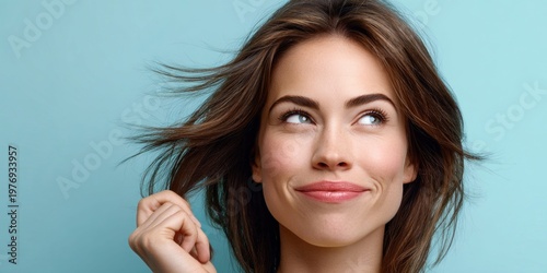 Young woman with flowing brown hair and blue eyes smiles coyly against a teal background