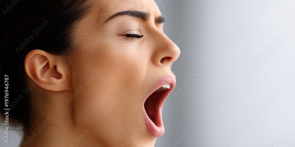 Fototapeta premium Close-up profile of a woman yawning widely with her eyes closed and mouth open