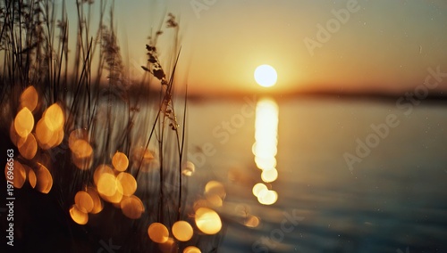 Golden sunset over calm water with blurred foreground grass and sparkling bokeh lights