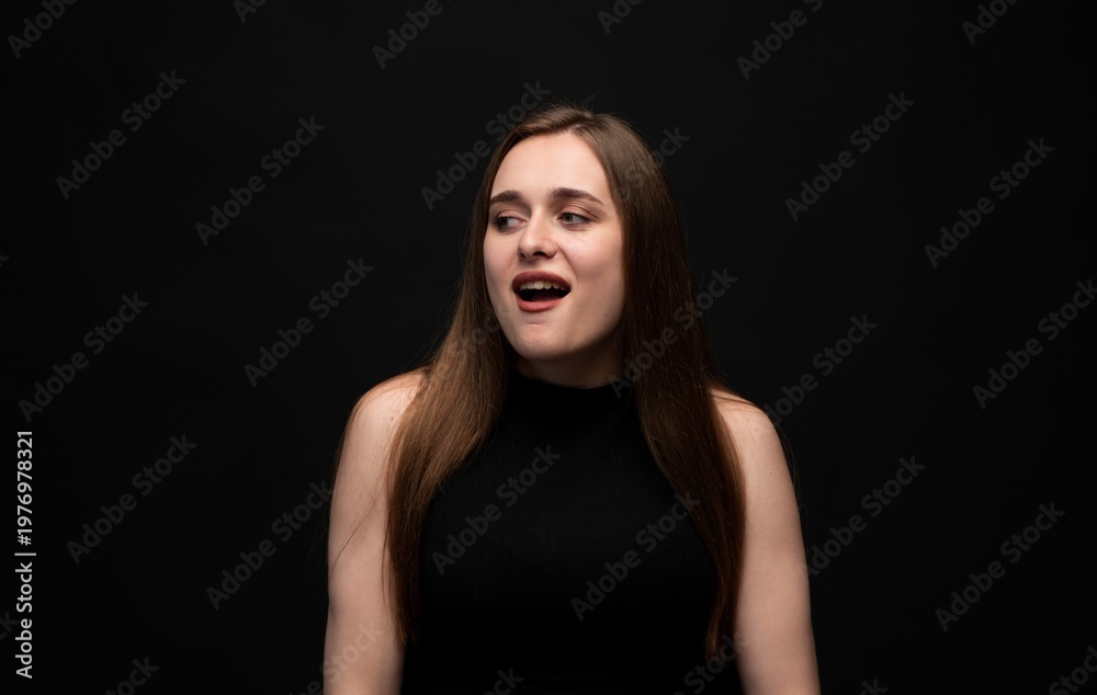 Naklejka premium Young woman looking away with open mouth expressing curiosity, surprise or disgust on a black background
