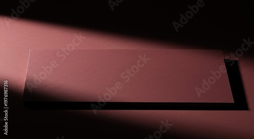 A sharp, dark shadow falls across a minimalist, textured surface, defining an empty rectangular shape that serves as a visual placeholder or background, minimalism, visualization, mystery