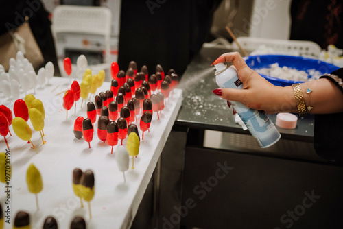 Close-up of handmade polymer clay craft. Female hand spraying paint on colorful miniature clay objects in workshop. Concept of DIY, artisan craft, hobby and small business production.