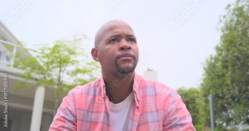 Camera pulling back, African man in plaid sitting up, looking off-frame and smiling by glass doors