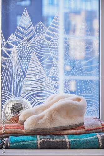 Cozy winter window scene with soft slippers and plaid blankets