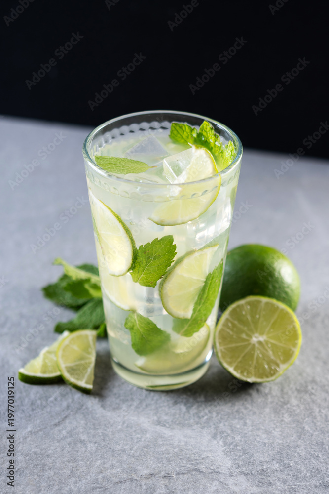 Fototapeta premium Fresh mojito cocktail with lime, mint and ice in glass on gray surface and black background. 