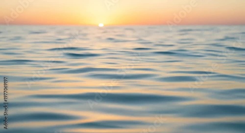 Sunset over tranquil sea with soft ripples and a glowing sun on the horizon