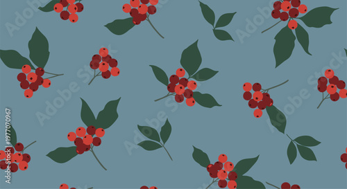 Beautiful seamless pattern of red rowan berries and green leaves scattered on a muted blue background for autumn and winter themed design projects.