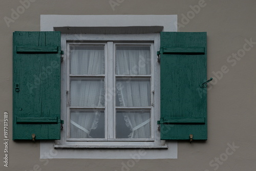 Window with turquoise shutters on neutral plaster wall