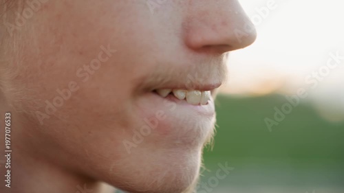 White young man smiling playfully at sunset, lip movement and light tongue gesture, freckled chin with light stubble, closeup mouth and jaw, relaxed friendly mood, warm natural light, candid outdoor