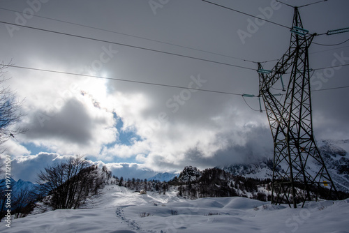 Snow covered mountains with power line tower and clouds