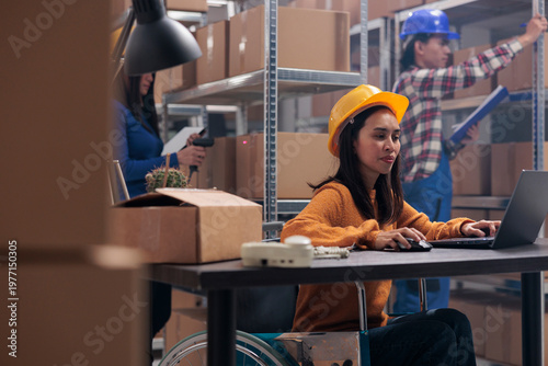 Принти на полотні Asian postal service worker with physical disability using laptop in warehouse