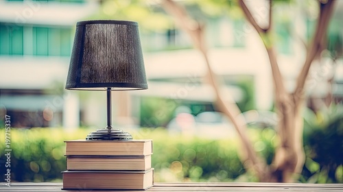 Small electric lamp rests atop a stack of reading materials upon a wooden surface outdoors.