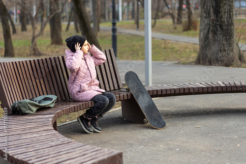 Young girl sitting on a park bench with her skateboard nearby, resting after an active day.