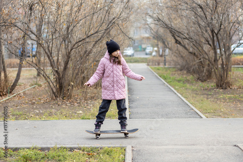 Full length portrait of a young girl standing on a skateboard in the middle of an autumn park alley.