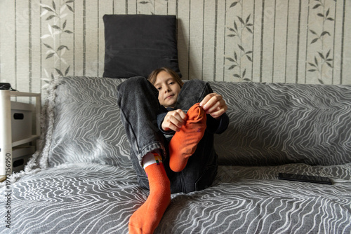 A young girl sitting on a patterned sofa and putting on bright orange socks, preparing to go out.