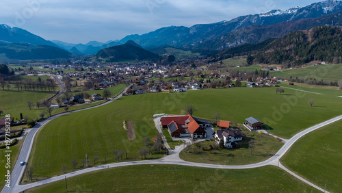 Aerial view of emerald fields unfurl towards the village nestled in the valley, framed by majestic mountains, Windischgarsten, Upper Austria, Austria.