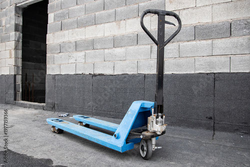 Blue hydraulic pallet truck positioned near an open doorway of a concrete block building under construction.