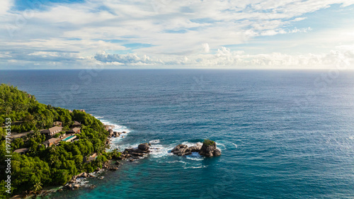A dense green forest covering a rocky coastline, with clear turquoise waters. Seychelles, Mahe.