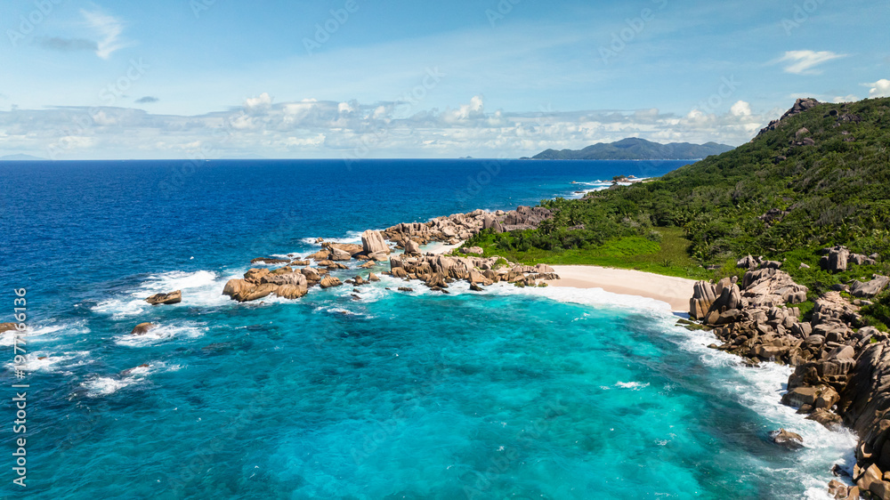 Fototapeta premium Granite coastline with clear turquoise waters, white sandy beach, and vibrant greenery. Anse Marron beach. La Digue, Seychelles.