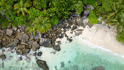 Clear emerald waters gently lapping against a sandy beach surrounded by lush greenery. Butzel Beach. Seychelles, Mahe.