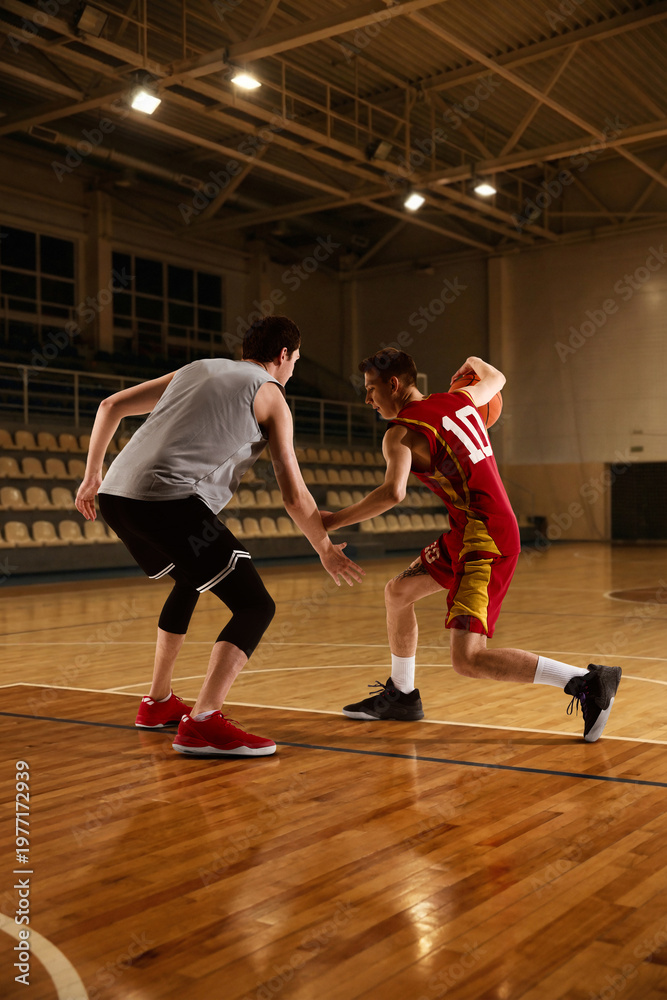 Fototapeta premium Two basketball players competing on indoor court during game action moment. Concept of sports rivalry, athletic performance, training session, active lifestyle, and professional game practice.